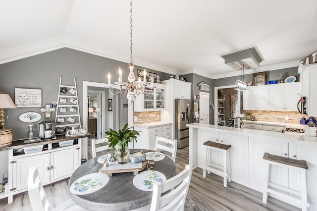 dining room featuring a notable chandelier, ornamental molding, vaulted ceiling, and light wood-type flooring