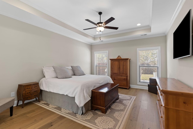 bedroom with ceiling fan, ornamental molding, a raised ceiling, and light hardwood / wood-style flooring