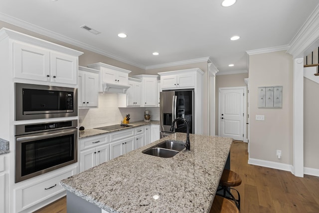 kitchen with appliances with stainless steel finishes, sink, white cabinets, dark wood-type flooring, and a center island with sink