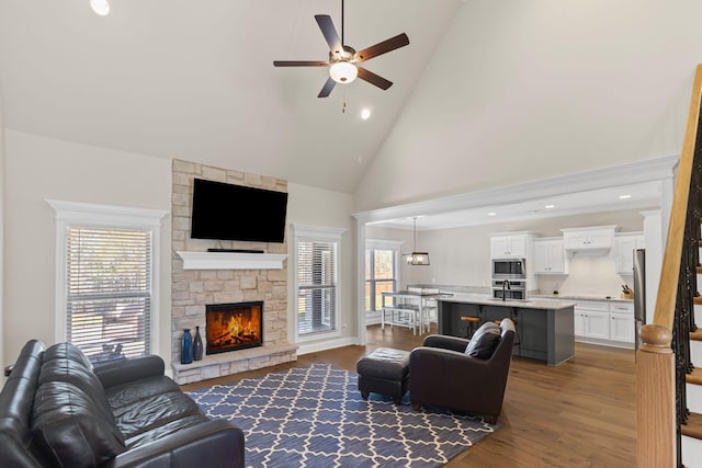 living room with a stone fireplace, sink, high vaulted ceiling, dark hardwood / wood-style floors, and ceiling fan