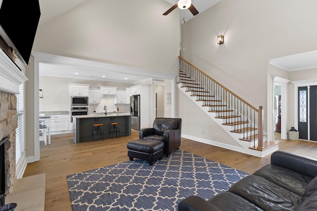 living room featuring high vaulted ceiling, a fireplace, sink, hardwood / wood-style flooring, and crown molding