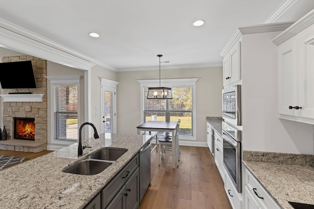 kitchen with sink, white cabinetry, stainless steel appliances, ornamental molding, and light stone countertops