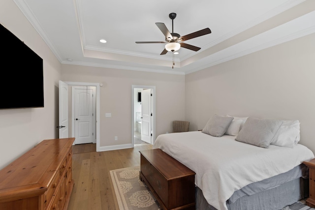 bedroom featuring a tray ceiling, ornamental molding, light hardwood / wood-style floors, and ensuite bath