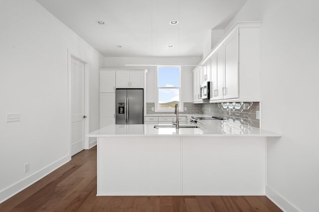 kitchen with sink, kitchen peninsula, stainless steel appliances, decorative backsplash, and white cabinets