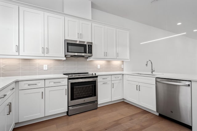 kitchen with sink, white cabinetry, backsplash, stainless steel appliances, and light wood-type flooring