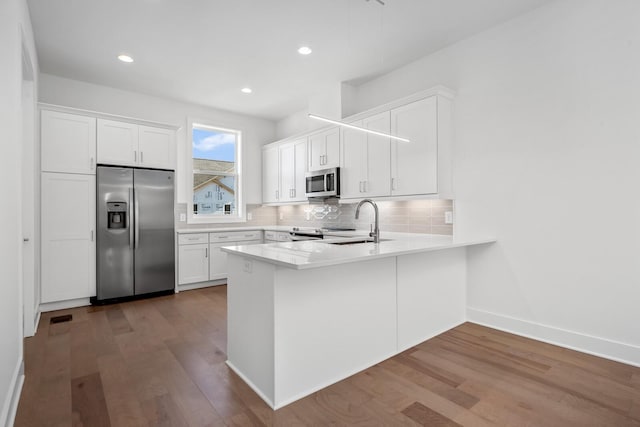 kitchen featuring sink, hardwood / wood-style flooring, stainless steel appliances, white cabinets, and decorative backsplash