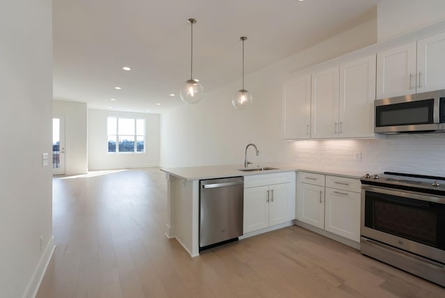 kitchen featuring appliances with stainless steel finishes, decorative light fixtures, white cabinets, decorative backsplash, and kitchen peninsula