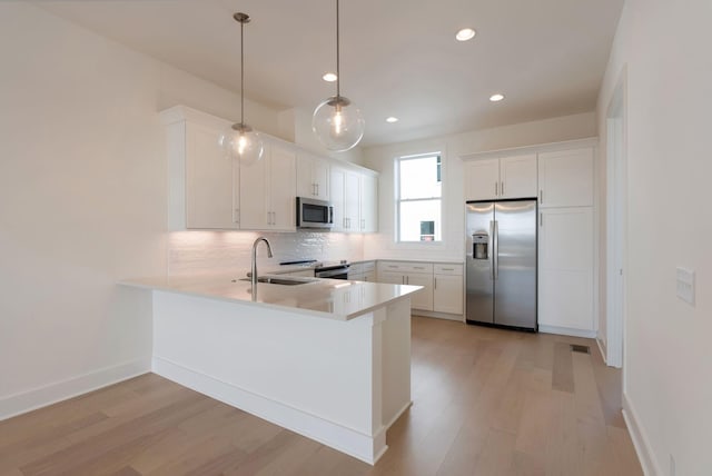 kitchen with appliances with stainless steel finishes, decorative light fixtures, sink, white cabinets, and kitchen peninsula