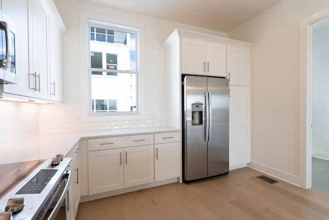 kitchen featuring stainless steel appliances, white cabinetry, backsplash, and light wood-type flooring