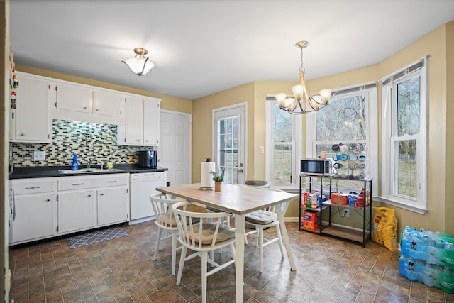 kitchen featuring pendant lighting, tasteful backsplash, sink, white cabinets, and white dishwasher