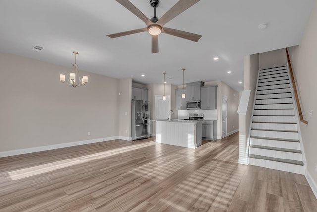 unfurnished living room with ceiling fan with notable chandelier, sink, and light wood-type flooring