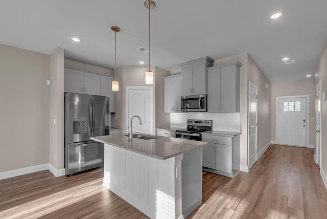 kitchen featuring pendant lighting, an island with sink, sink, stainless steel appliances, and light stone countertops