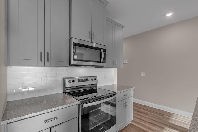 kitchen with stainless steel appliances, gray cabinetry, backsplash, and light hardwood / wood-style floors