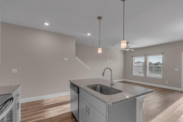 kitchen with appliances with stainless steel finishes, pendant lighting, an island with sink, sink, and light hardwood / wood-style flooring