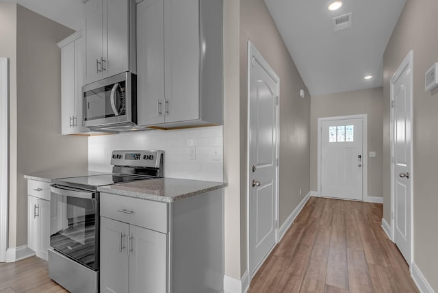 kitchen featuring light stone counters, backsplash, light hardwood / wood-style flooring, and stainless steel appliances