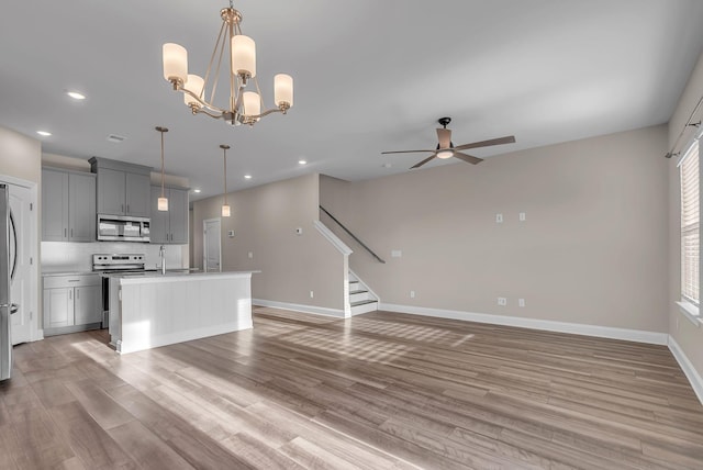 unfurnished living room featuring ceiling fan with notable chandelier and light hardwood / wood-style flooring