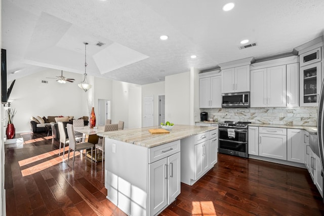 kitchen with decorative light fixtures, stainless steel appliances, white cabinets, and a kitchen island