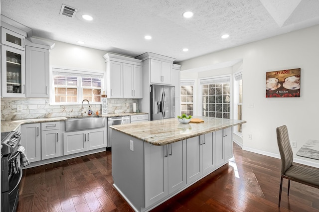 kitchen featuring appliances with stainless steel finishes, white cabinetry, sink, a center island, and light stone countertops