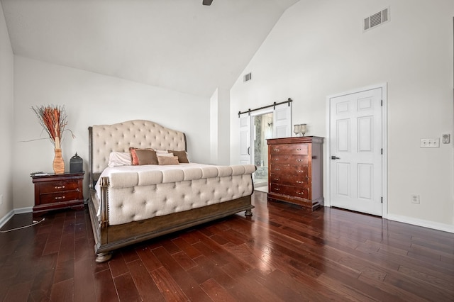 bedroom with dark hardwood / wood-style floors, a barn door, and high vaulted ceiling