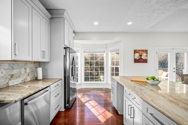 kitchen featuring white cabinetry, appliances with stainless steel finishes, light stone countertops, and backsplash