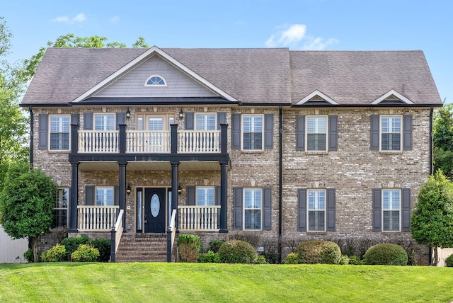 view of front of property featuring a front yard, covered porch, brick siding, and a balcony