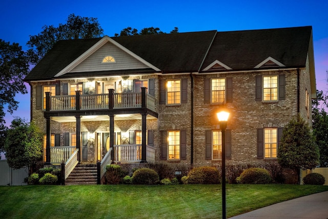 view of front of house with a porch, brick siding, a balcony, and a front lawn