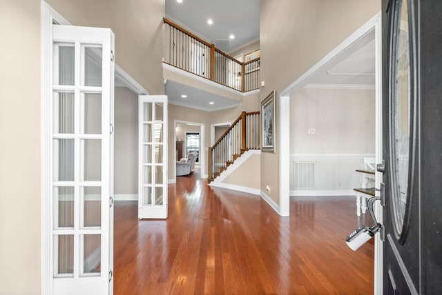 entryway with french doors, a towering ceiling, ornamental molding, and hardwood / wood-style flooring