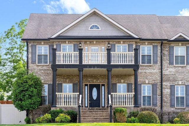 multi unit property featuring a balcony, roof with shingles, a porch, and brick siding