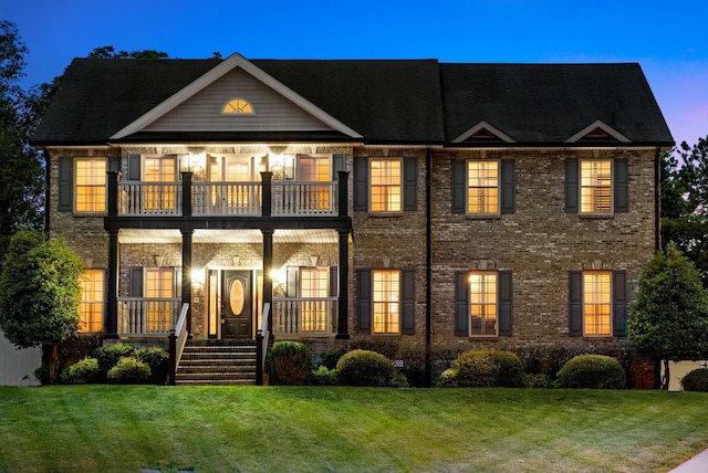 view of front of house with a porch, brick siding, a lawn, and a balcony