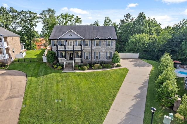 view of front of home with stone siding, fence, a balcony, and a front lawn