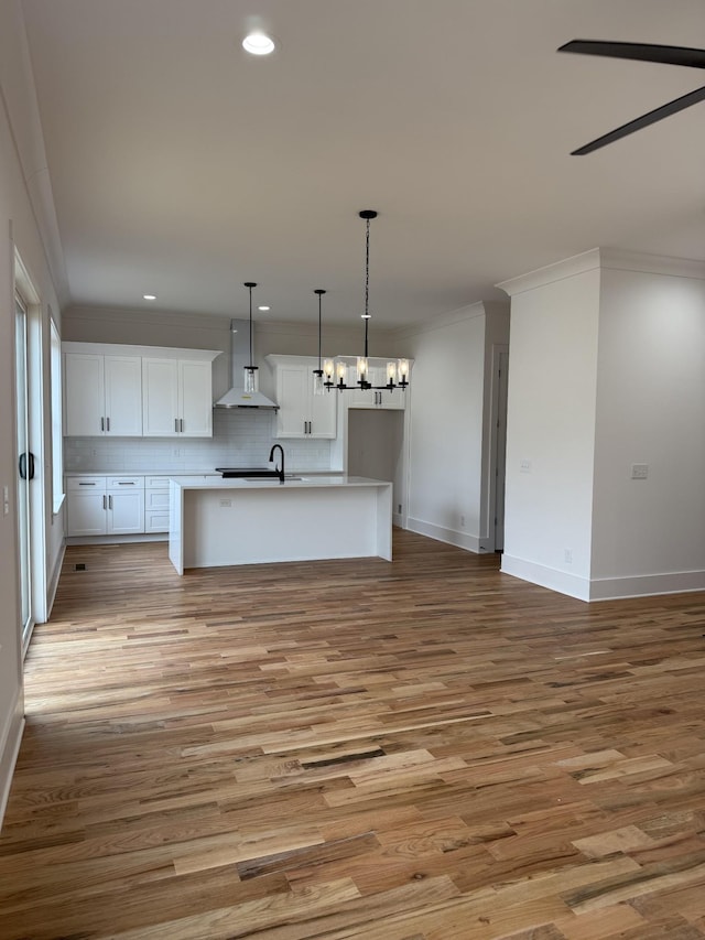 kitchen featuring a kitchen island with sink, decorative backsplash, white cabinets, decorative light fixtures, and wall chimney exhaust hood