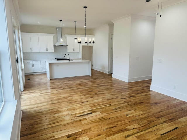 kitchen featuring a kitchen island with sink, sink, white cabinetry, and wall chimney exhaust hood