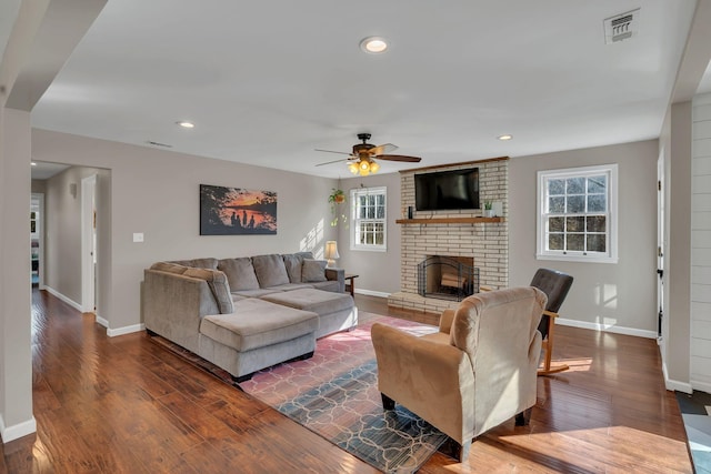 living room with a brick fireplace, dark hardwood / wood-style floors, and ceiling fan