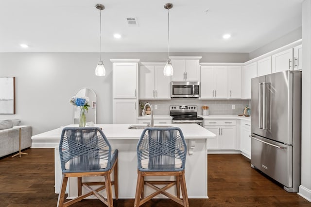 kitchen with white cabinetry, stainless steel appliances, an island with sink, and hanging light fixtures