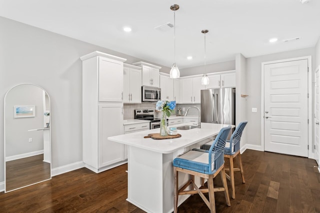 kitchen with decorative light fixtures, tasteful backsplash, white cabinetry, a kitchen island with sink, and stainless steel appliances