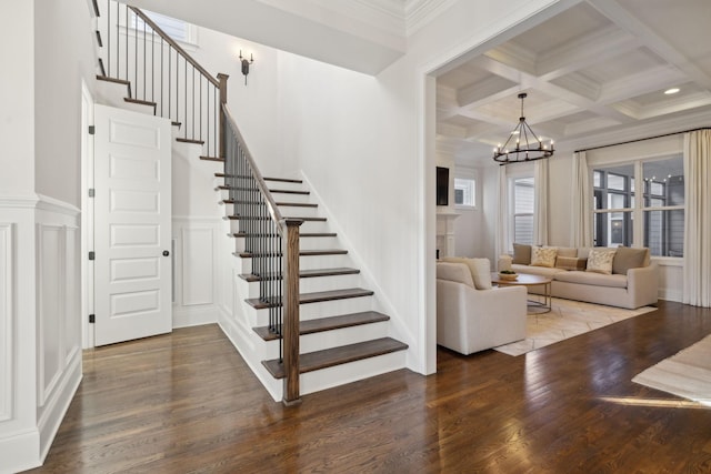 unfurnished living room featuring coffered ceiling, crown molding, a chandelier, beam ceiling, and hardwood / wood-style floors