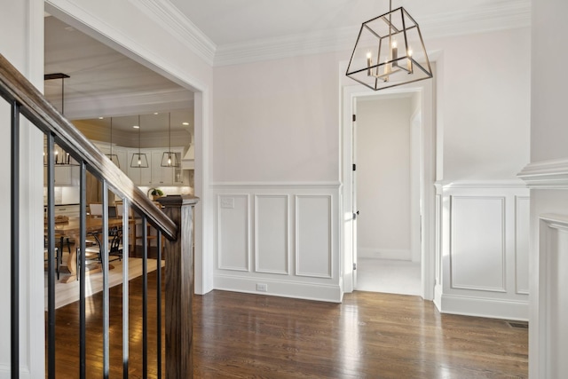 foyer entrance with dark wood-type flooring, ornamental molding, and an inviting chandelier