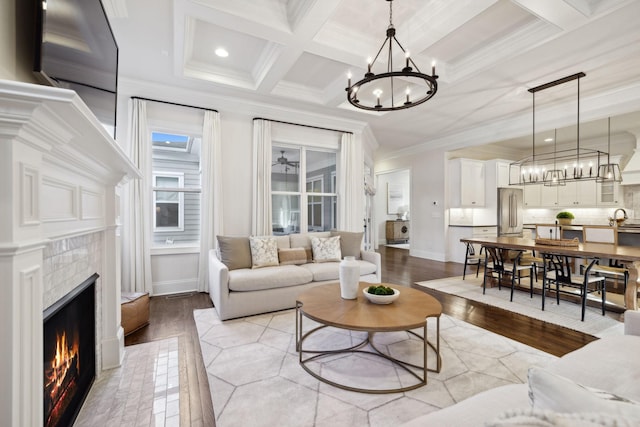 living room featuring a tiled fireplace, ornamental molding, coffered ceiling, beam ceiling, and light hardwood / wood-style flooring