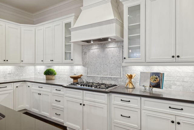 kitchen featuring premium range hood, stainless steel gas stovetop, white cabinets, backsplash, and ornamental molding