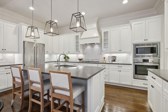 kitchen with sink, appliances with stainless steel finishes, hanging light fixtures, a center island with sink, and custom exhaust hood