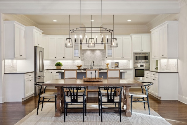 kitchen featuring dark wood-type flooring, appliances with stainless steel finishes, decorative light fixtures, and white cabinets