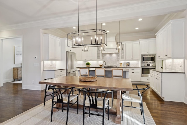 kitchen featuring appliances with stainless steel finishes, decorative light fixtures, an island with sink, white cabinets, and custom exhaust hood