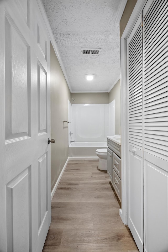 full bathroom with hardwood / wood-style floors, vanity, ornamental molding, toilet, and a textured ceiling