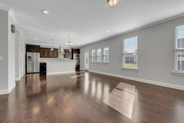 unfurnished living room with an inviting chandelier, crown molding, dark wood-type flooring, and a healthy amount of sunlight