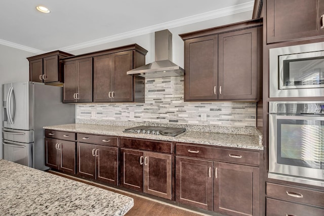 kitchen featuring wall chimney range hood, appliances with stainless steel finishes, dark brown cabinetry, ornamental molding, and light stone countertops