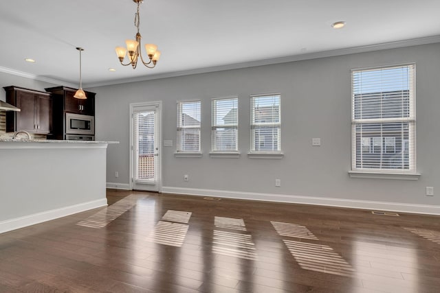 unfurnished living room with dark hardwood / wood-style flooring, ornamental molding, a healthy amount of sunlight, and an inviting chandelier