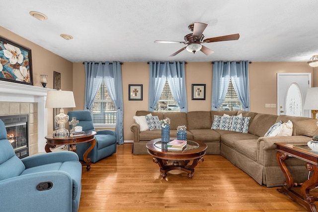 living room with a tiled fireplace, ceiling fan, a textured ceiling, and light wood-type flooring