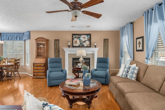 living room with ceiling fan, a tiled fireplace, hardwood / wood-style floors, and a textured ceiling