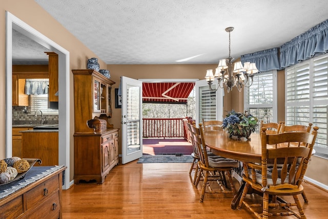 dining space with sink, a textured ceiling, light hardwood / wood-style flooring, and a chandelier