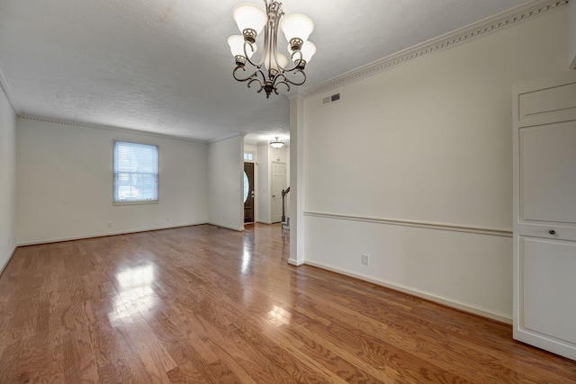 spare room featuring crown molding, a textured ceiling, a notable chandelier, and light hardwood / wood-style floors